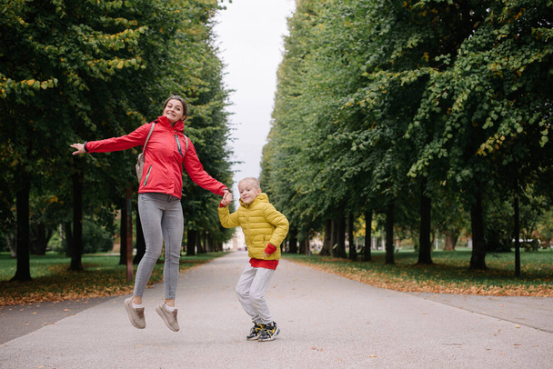 Mother and son jumping in the autumn park. Fall Season. Happy young beautiful mother and her son have a walk in the park - Zdjęcie, obraz
