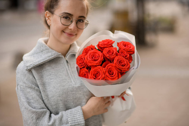 happy handsome young woman with bouquet of bright red roses in wrapping paper in her hands - Φωτογραφία, εικόνα