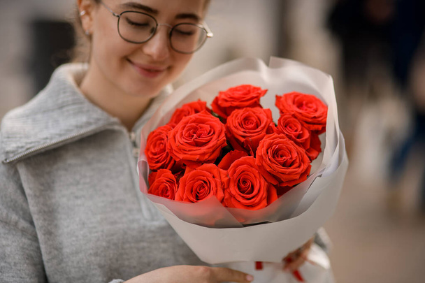 Close-up of happy handsome young woman with bouquet of bright red roses in wrapping paper in her hands - Foto, Imagem