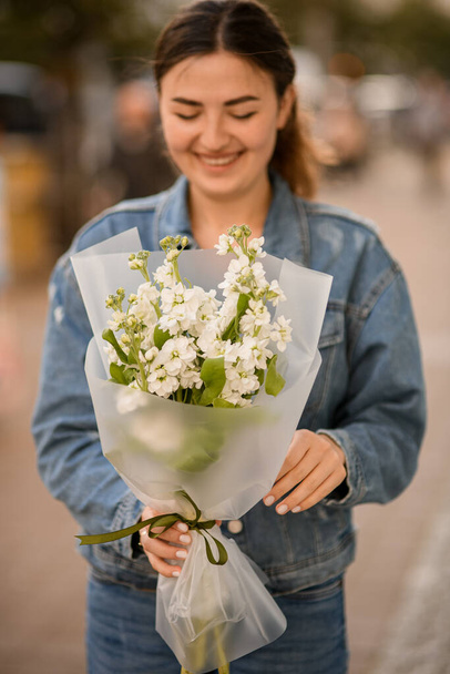 young beautiful smiling woman holds in her hand a bouquet of fresh white matthiola flowers - Фото, изображение