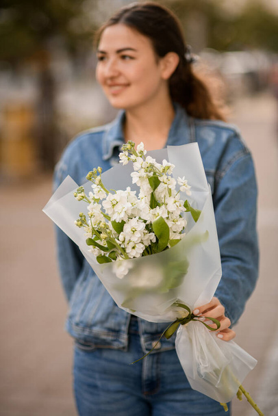 Selective focus on bouquet of fresh white matthiola flowers in hand of beautiful smiling woman - Valokuva, kuva