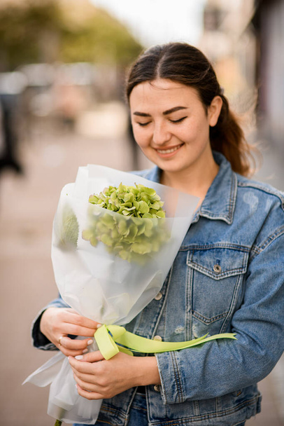 Great view on young attractive woman with elegant trendy bouquet of green hydrangea in wrapping paper in her hands - Fotó, kép