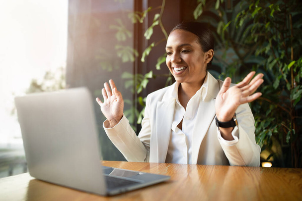 Szczęśliwy zaskoczony młoda czarna kobieta w garniturze patrząc na laptopa, gestykulując dłońmi w nowoczesnej eko kawiarni z wnętrza zielonych roślin. Szokująca oferta i reklama, dobre wieści, praca i biznes zdalnie - Zdjęcie, obraz
