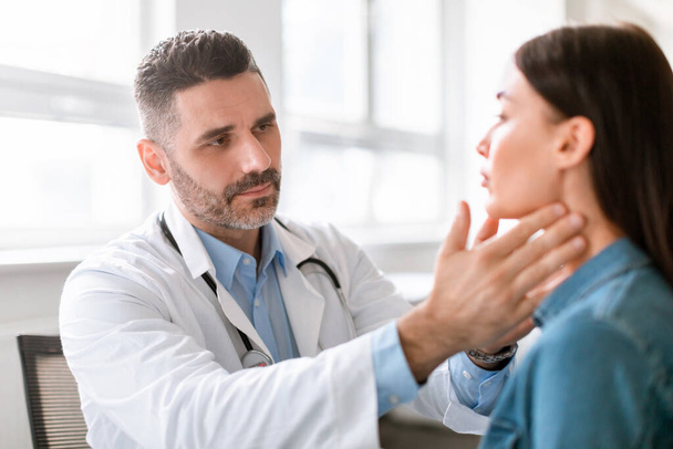 Medicine, healthcare and medical check up concept. Male doctor checking patients tonsils at hospital. Endocrinologist examining throat of young lady in clinic - Foto, immagini