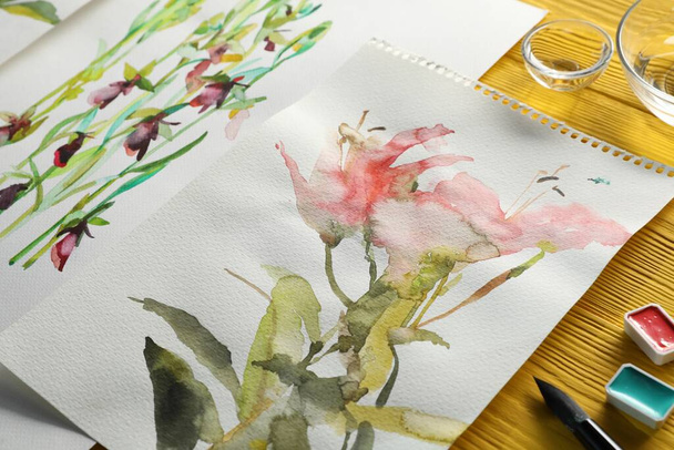 Beautiful floral pictures and watercolor paints on yellow wooden table - Valokuva, kuva