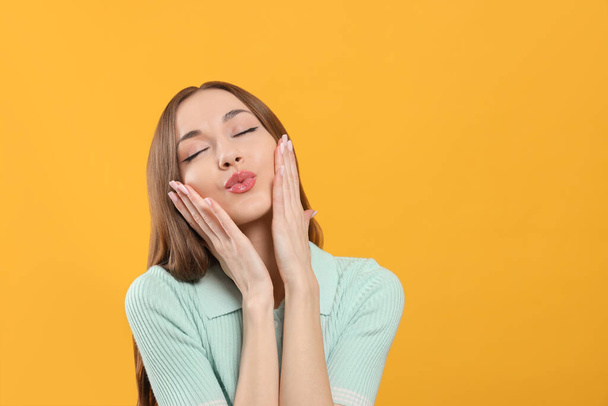 Beautiful young woman blowing kiss on yellow background, space for text - Foto, afbeelding