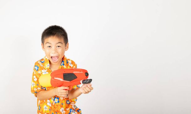 Happy Songkran Day, Asian kid boy with floral shirt hold water gun, Thai child funny hold toy water pistol and smile, isolated on white background, Thailand Songkran festival national culture concept - Photo, image
