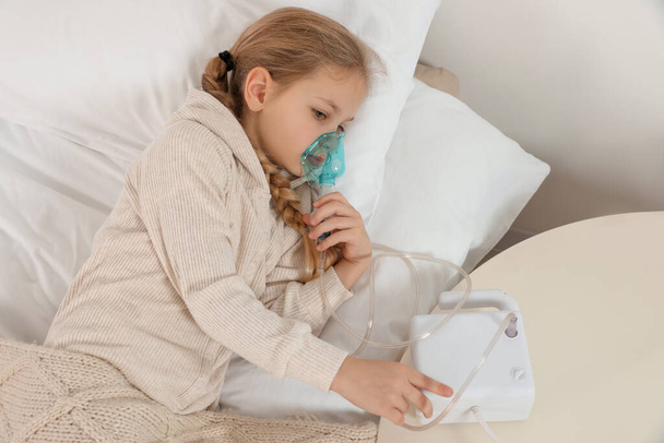 Little girl using nebulizer for inhalation on bed indoors - Foto, afbeelding