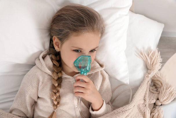 Little girl using nebulizer for inhalation on bed indoors, top view - Foto, imagen