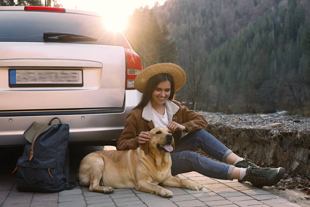 Happy woman and adorable dog sitting near car in mountains. Traveling with pet - Valokuva, kuva