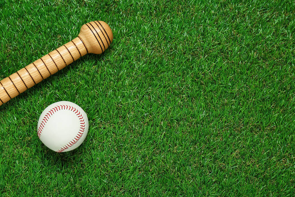 Wooden baseball bat and ball on green grass, flat lay. Space for text - Foto, afbeelding