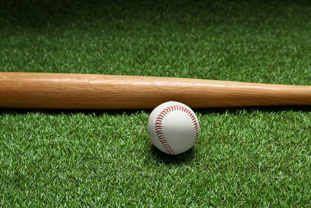 Wooden baseball bat and ball on green grass. Sports equipment - Photo, image