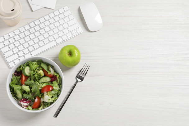 Bowl of tasty food, keyboard, apple and fork on white wooden table, flat lay with space for text. Business lunch - Photo, image