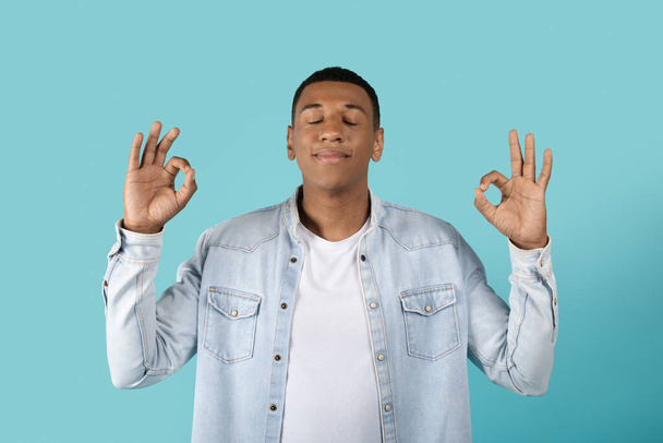 Ruhige Millennial Black Guy meditiert mit geschlossenen Augen, träumt, genießt Freizeit, Stille und Frieden isoliert auf blauem Studiohintergrund. Gesundheitsfürsorge, entspannen, ausruhen und eine Pause einlegen - Foto, Bild