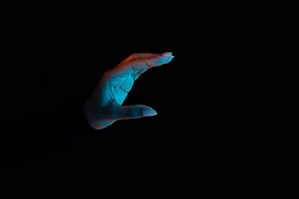 Fekete női kéz kezében láthatatlan tárgy, mutató kis mennyiségű valamit, vagy kezében valamit, fekete háttér neon fények. Panoráma fénymásoló felülettel - Fotó, kép