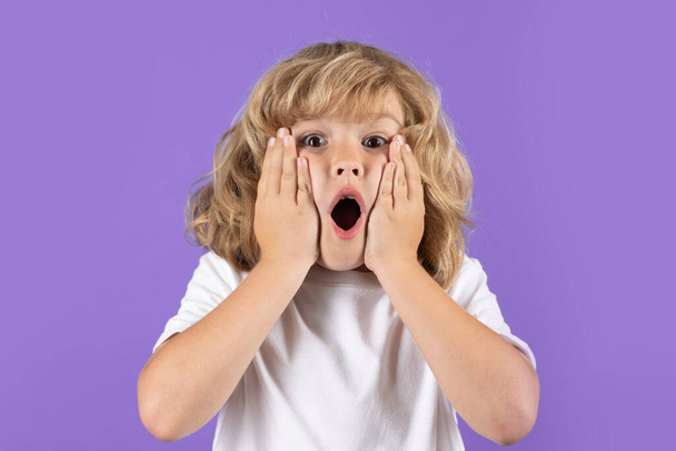 Shocked kid boy keeping hands near cheek with open mouth on studio isolated background. Surprised face, excited emotions of child. Shock, omg and wow expression - Foto, Imagen
