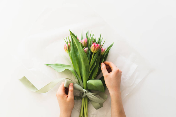 Womans hands holding bouquet of beautiful delicate tulip flowers on white background. Bouquet of pink fresh tulips. - Photo, image