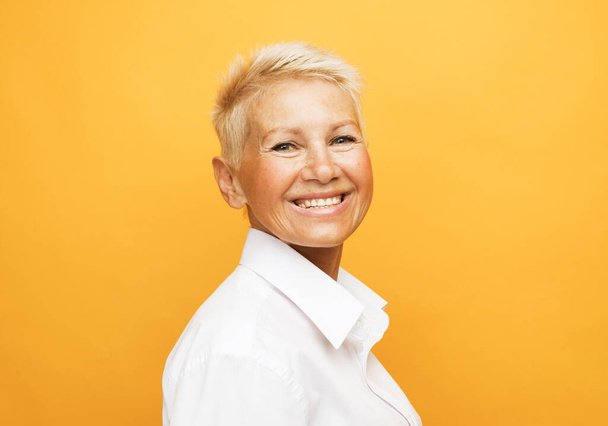 Life only starts when get older. Portrait of charming happy and carefree european senior woman with blond short hair laughing over yellow background - Фото, зображення