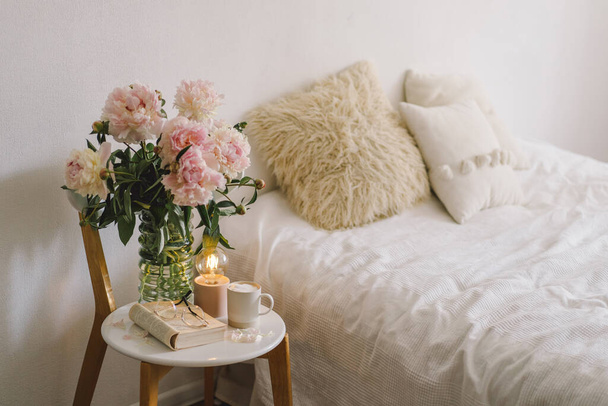 Натюрморты в домашнем интерьере гостиной. Открытая книга с очками, чашечкой кофе и букетом белых розовых пионов цветы. Читай и отдыхай. Уютный дом - Фото, изображение