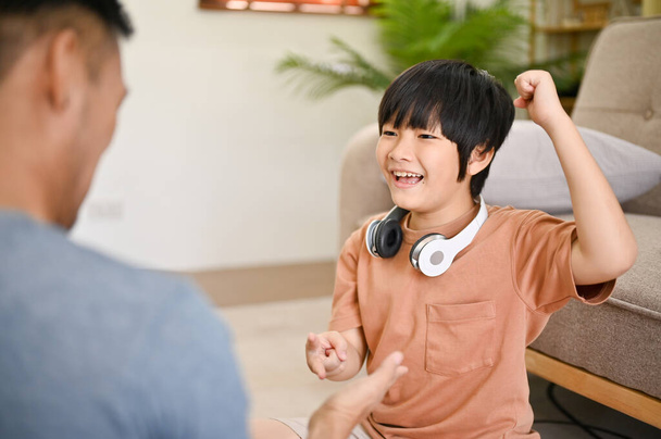 lindo y feliz asiático pequeño niño jugando piedra papel tijeras con su papá, pasando diversión familia juegos tiempo en la sala de estar juntos. - Foto, imagen