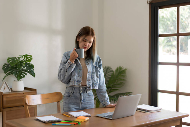 Concepto de diseño creativo, diseñadora femenina bebiendo café mientras trabaja y buscando datos en el portátil. - Foto, imagen