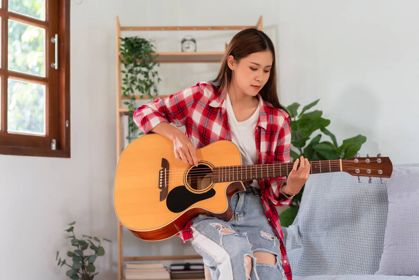 Concepto de relajación con música, Mujer asiática joven practica tocar acordes con guitarra acústica. - Foto, Imagen