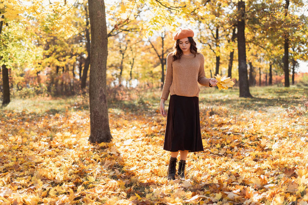 Pretty young elegant woman in a beret with a beautiful smile walks in a park among trees with orange foliage. Modern cheerful girl hipster in the forest. Copy space - Photo, Image