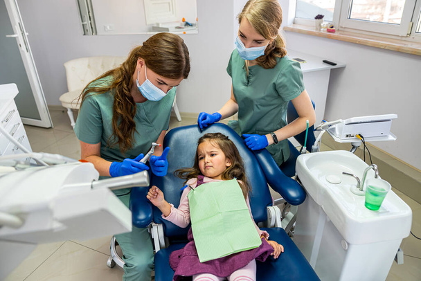 jovem dentista especialista qualificado mulher escovar os dentes de uma criança pequena que foi trazido para a recepção. O conceito de escovar os dentes de leite - Foto, Imagem
