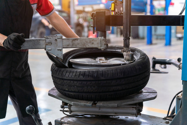 A male car mechanic changing tires and balancing car wheel on balancer at auto repair shop for the auto industry. Automobile industry. Machine for removing rubber from the wheel disc. - Photo, Image