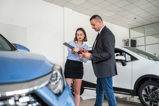 Female dealer in suit holding clipboard help with purchase new car her client, selling concept - Photo, Image