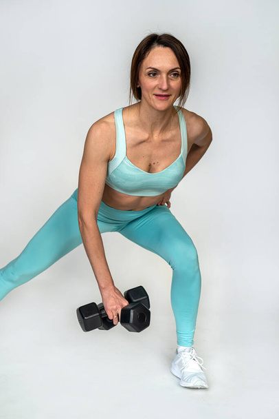 Sporty woman doing exercises with metal dumbbells training against the background of a plain white wall. Photo of a muscular woman in sportswear on a white background. Strength and motivation. muscles - Photo, image