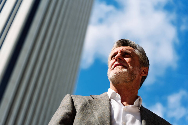 Низкоугловой портрет бизнесмена в элегантной одежде, стоящего возле финансового здания - Фото, изображение