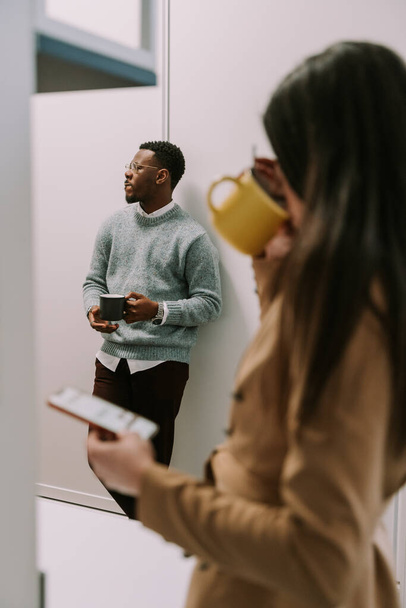 Egy fiatal barna nő kávét iszik szünetben, miközben a fekete férfi kollégája hallgatja a munkatársait. - Fotó, kép