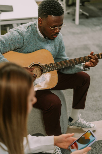 Красива чорношкіра людина грає на гітарі в офісі для своїх колег в кінці зміни
 - Фото, зображення