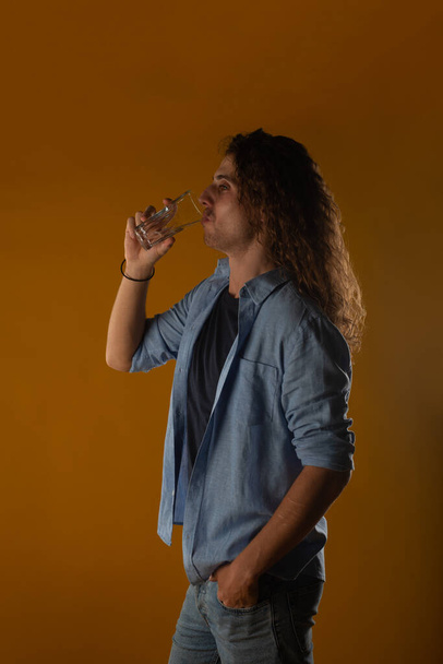 Sopiva ja komea nuori mies poseeraa ja juo lasillisen vettä studiossa - Valokuva, kuva