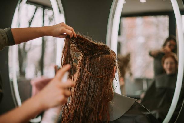 Close up de cabeleireiro colocando algum spray em seus clientes cabelo vermelho no salão de cabeleireiro - Foto, Imagem