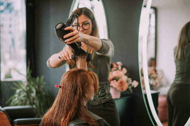 Блондинка парикмахер дуть сушить волосы своих клиентов в парикмахерской - Фото, изображение