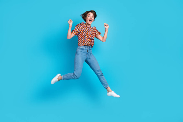 Full size portrait of delighted pretty girl jumping raise fists shout yes hooray isolated on blue color background. - Foto, Imagem