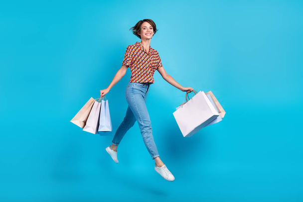 Full size profile photo of gorgeous carefree girl jumping hold shop bags isolated on blue color background. - Valokuva, kuva