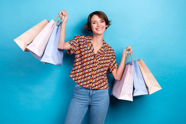 Photo of funny pretty lady dressed print shirt arms chest smiling rising shoppers isolated blue color background. - Foto, imagen