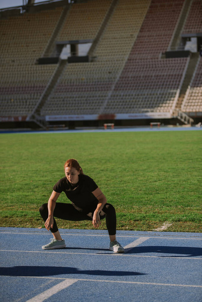 A beautiful woman is doing squats at the stadium, on a beautiful sunny morning - Foto, immagini
