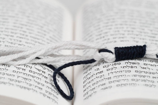 Black and white tzitzit knotted in the Sephardi style on a Torah.  Religious symbol.  - Photo, Image