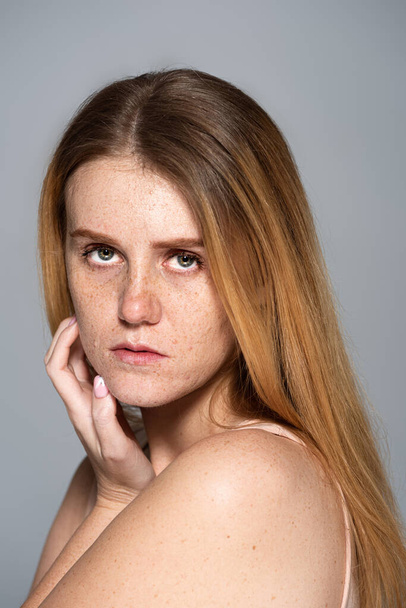 Портрет веснушчатой модели с кожей, смотрящей на камеру, изолированную на сером  - Фото, изображение