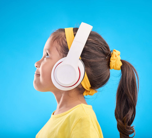 Música, fones de ouvido e ouvir com a menina em estúdio para streaming, rádio móvel e áudio. Tecnologia, mídia e juventude com perfil de criança isolada em fundo azul para natural, feliz e canções. - Foto, Imagem