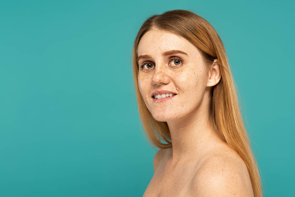 Positive Frau mit sommersprossiger Haut und nackten Schultern, die isoliert auf Türkis steht - Foto, Bild