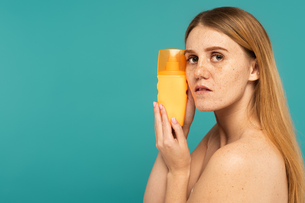 Молодая женщина с веснушками на коже держит солнцезащитный крем изолирован от бирюзы - Фото, изображение