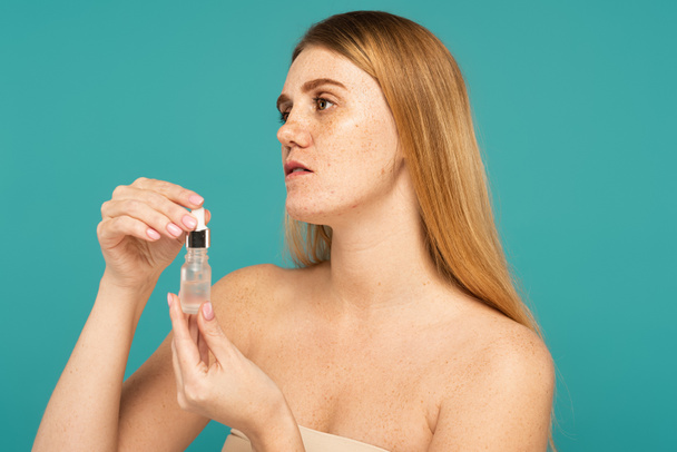 Young woman with freckles holding serum in bottle isolated on turquoise - Foto, afbeelding