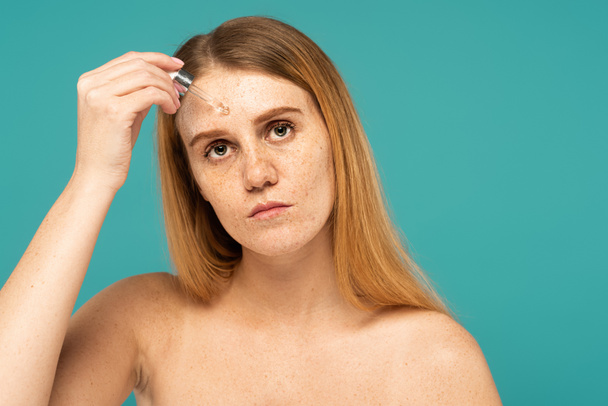 Woman with freckled skin applying serum on forehead with dropper isolated on turquoise - Foto, Bild