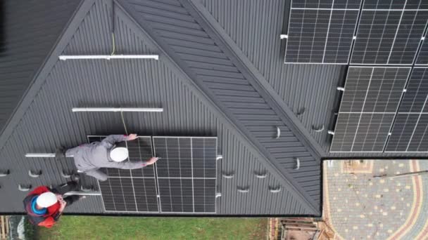 Τεχνικοί εγκαθιστούν φωτοβολταϊκά ηλιακά πάνελ στην οροφή του σπιτιού. Κηφήνας άποψη των μηχανικών ανδρών σε κράνη κτίριο ηλιακό σύστημα ενότητας με τη βοήθεια του δεκαεξαδικού κλειδιού. Έννοια της εναλλακτικής, ανανεώσιμης ενέργειας. - Πλάνα, βίντεο