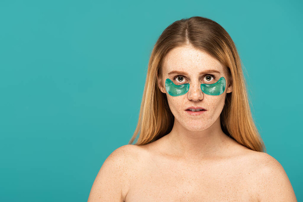 redhead woman with freckles and patches under eyes looking at camera isolated on turquoise  - Photo, Image
